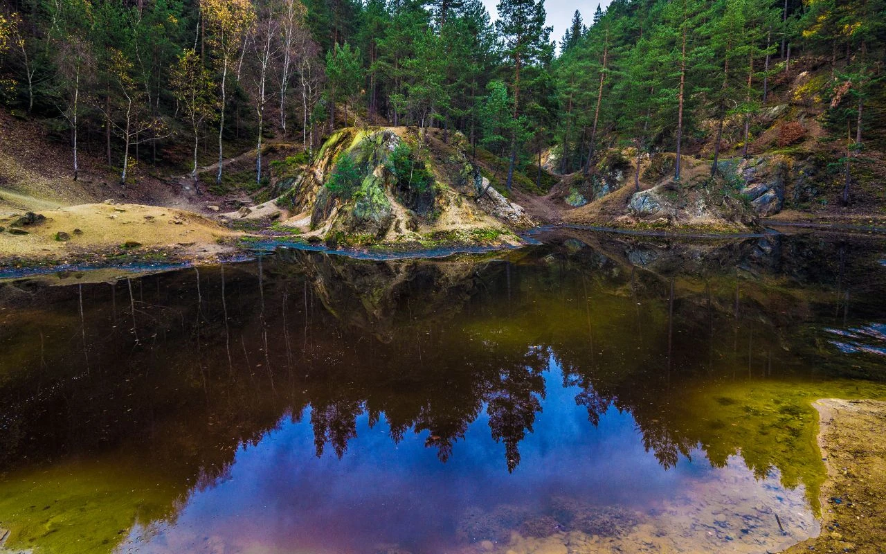 Kolorowe Jeziorka Malowniczy staw otoczony lasem iglastym z odbijającym się w wodzie niebem oraz skalistymi brzegami porośniętymi mchem i drobnymi drzewami.