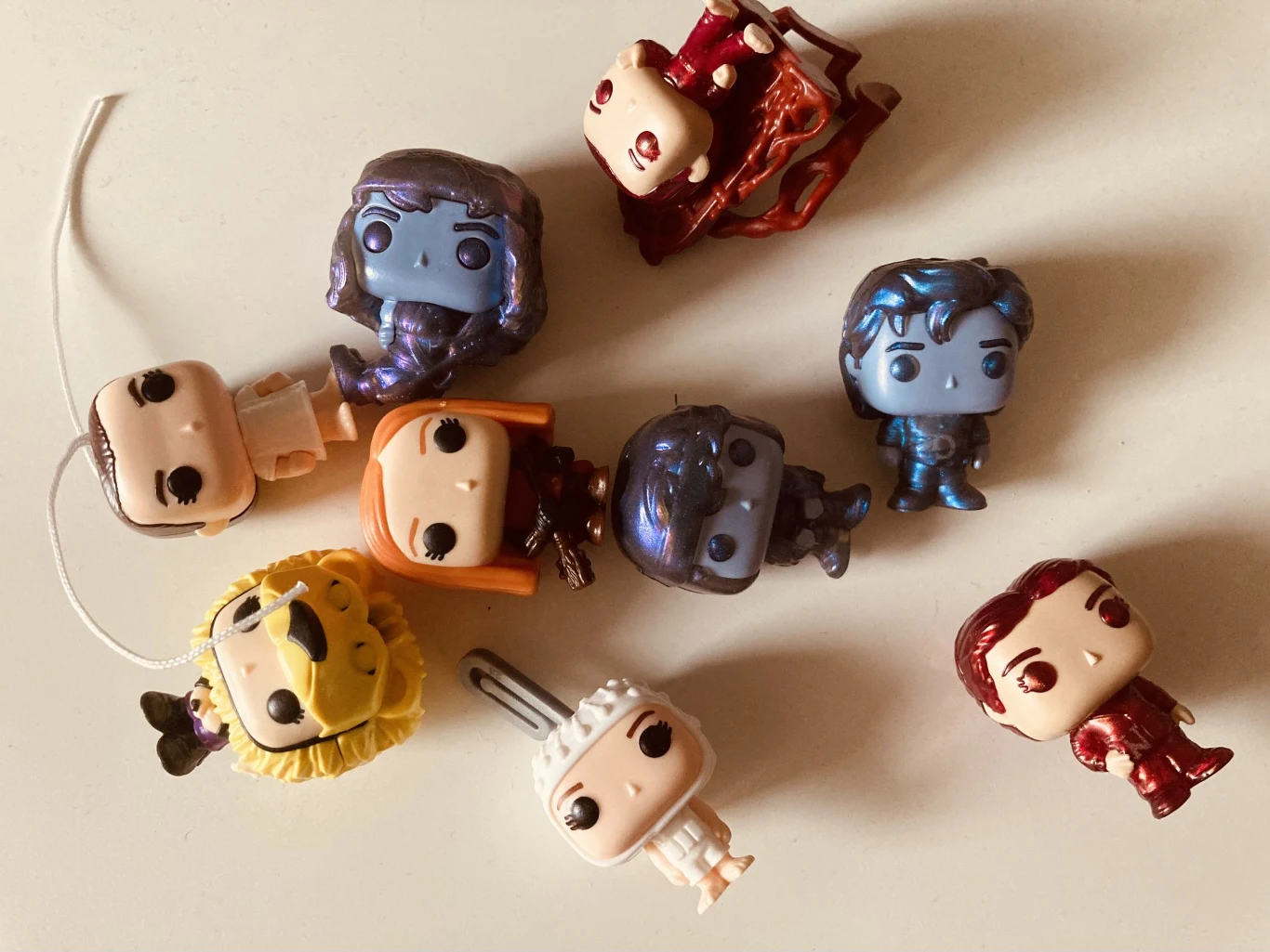 Kilka figurek typu Funko Pop z dużymi głowami przedstawiających różnorodne postacie w kolorowych strojach leży na jasnym tle.