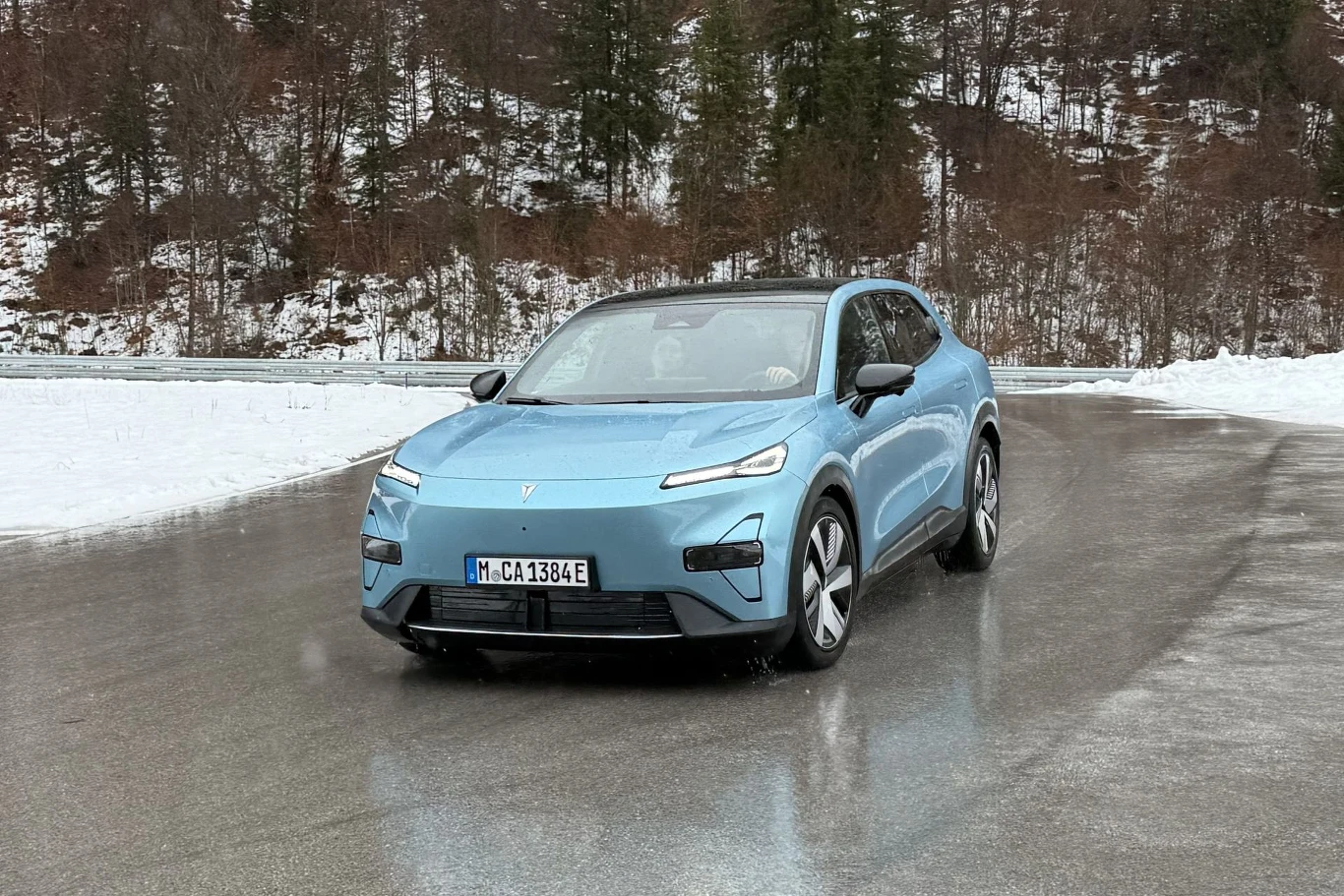 Changan Deepal S05 dzięki akumulatorowi znajdującemu się w podłodze jest dość zwarty w czasie pokonywania zakrętów. Jasnoniebieski nowoczesny samochód elektryczny jedzie po mokrej, zaśnieżonej drodze z otaczającym go zimowym krajobrazem oraz drzewami i ośnieżonymi wzgórzami w tle.