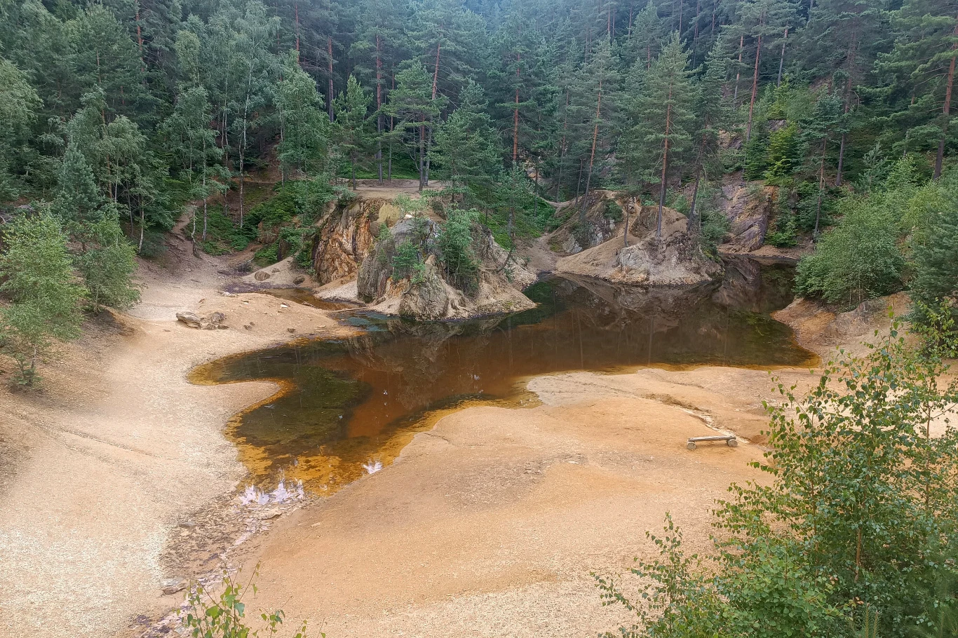 W Sudetach wiosną można podziwiać malownicze Kolorowe Jeziorka Małe, płytkie jezioro otoczone drzewami iglastymi i piaszczystymi brzegami, z widocznymi stromymi skarpami pokrytymi roślinnością.
