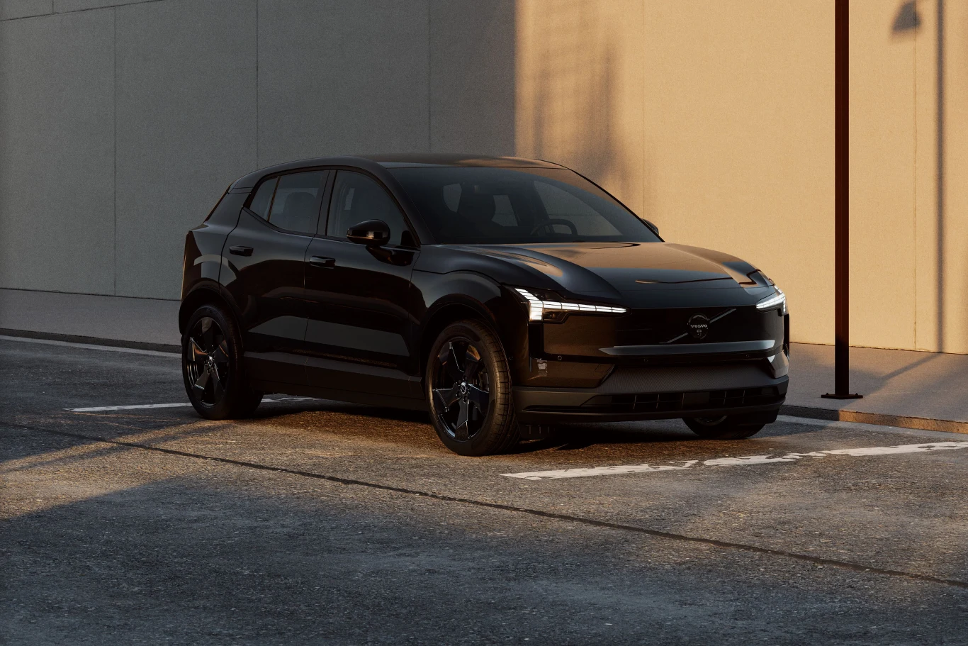 Czarny samochód osobowy typu SUV zaparkowany przy krawężniku na pustej ulicy, w tle jasny, gładki mur oświetlony światłem słonecznym i latarnia uliczna.