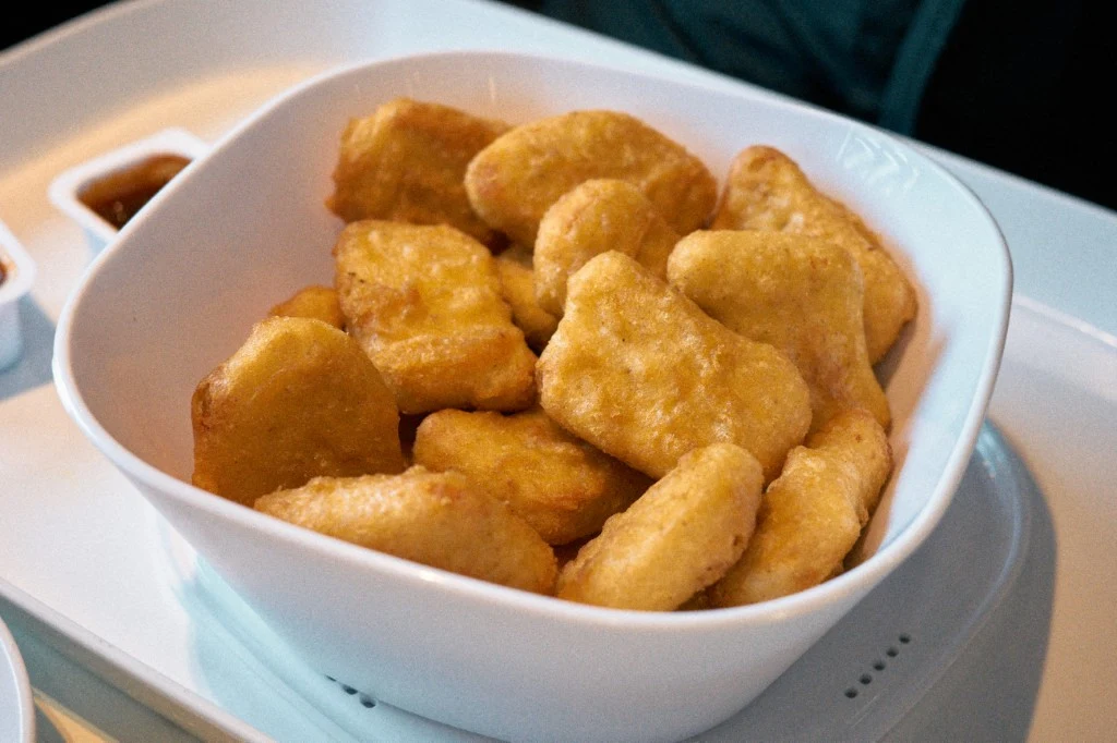 Miska wypełniona porcją złocistych, chrupiących nuggetów z kurczaka, obok na tacy widoczne sosy do maczania.