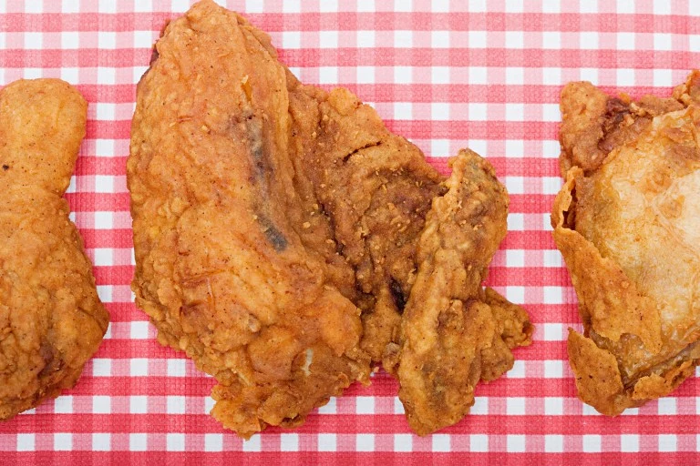 Kawałki chrupiącego, złocistego smażonego kurczaka ułożone na czerwono-białym obrusie w kratkę.