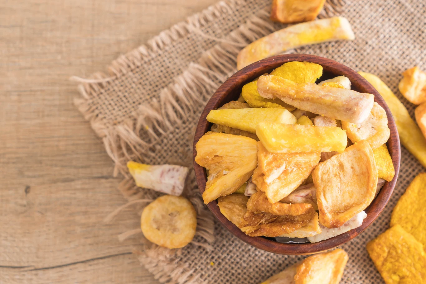 Suszony chlebowiec smakuje jak ananas lub banan Miska wypełniona chrupiącymi, suszonymi kawałkami egzotycznych owoców, ułożona na płóciennej serwetce na drewnianej powierzchni.