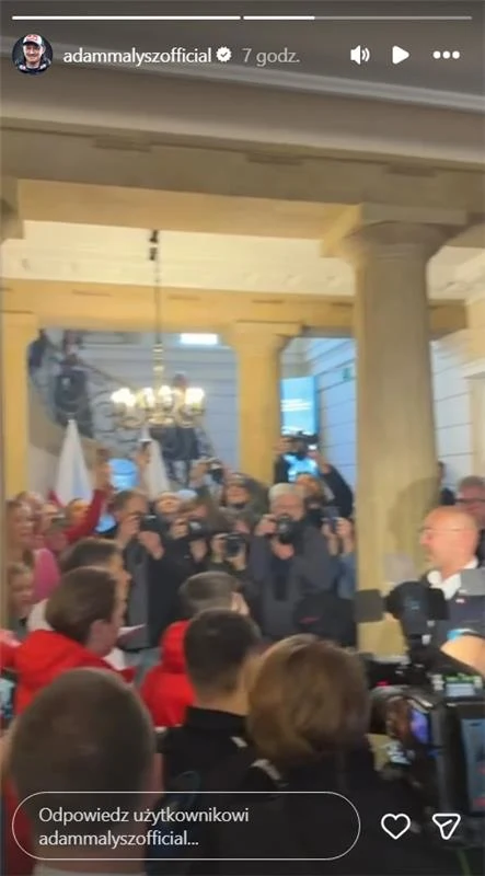 Jakub Rutnicki witał sportowców w ministerstwie Tłum ludzi, w tym fotoreporterzy z aparatami i kamery, zgromadzony wokół osoby rozmawiającej z grupą, w tle widoczne są jasne kolumny i żyrandol.