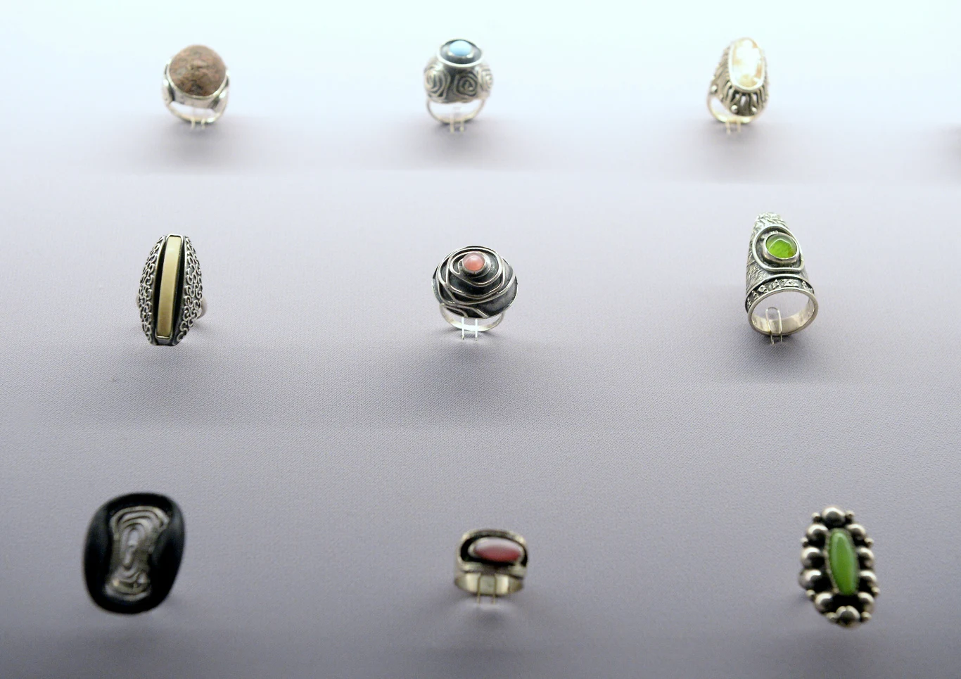 Kolekcja pierścionków z różnych materiałów, w tym srebrnych z kolorowymi kamieniami, ustawionych w równych rzędach na jasnym tle.