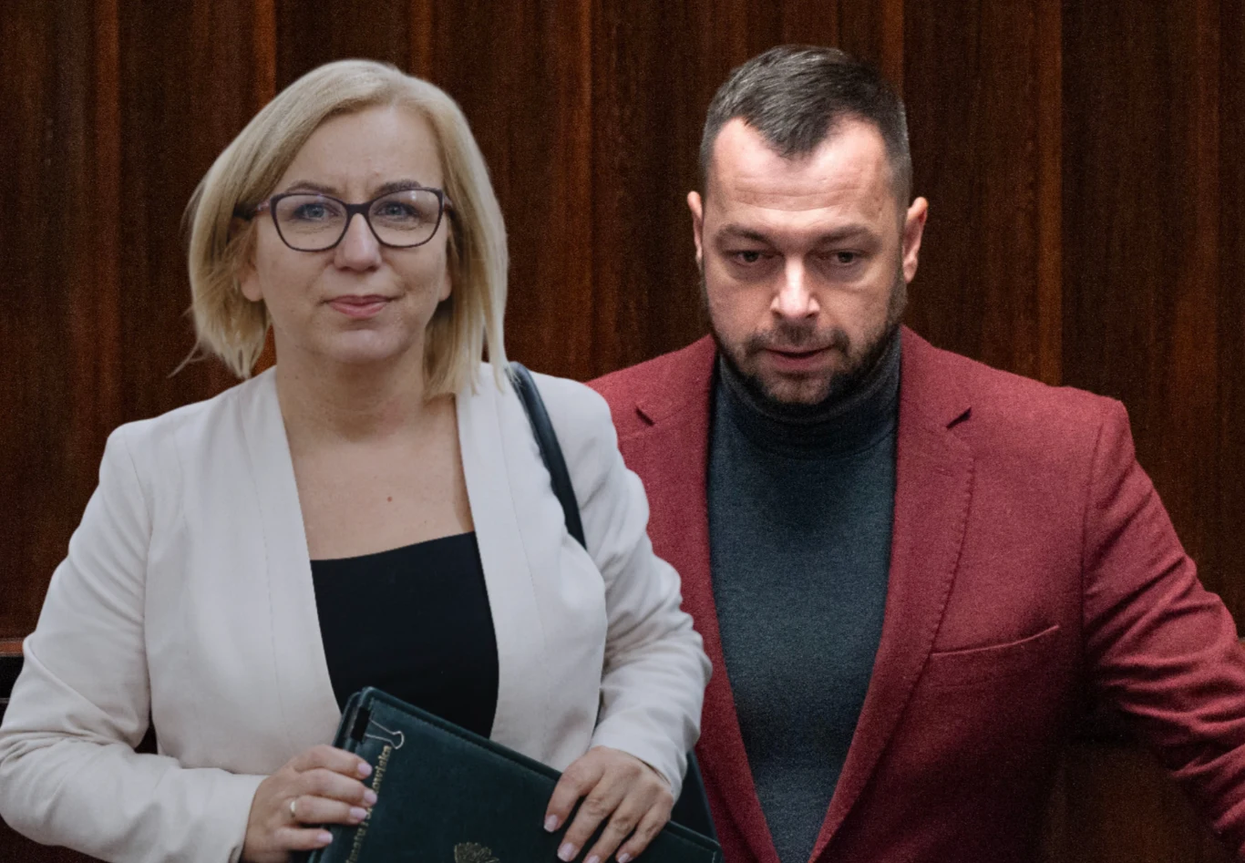 Paulina Hennig-Kloska i Bartosz Romowicz Kobieta w okularach i jasnej marynarce stoi obok mężczyzny w bordowej marynarce i ciemnym golfie na tle drewnianej ściany.