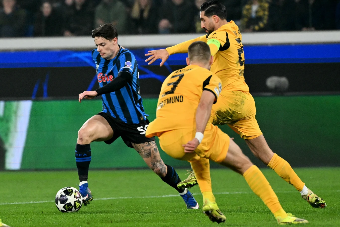 Nicola Zalewski w meczu z BVB Dwóch piłkarzy w żółtych strojach z drużyny Borussia Dortmund próbuje zatrzymać zawodnika w niebiesko-czarnej koszulce z piłką, dynamiczna akcja na tle stadionu pełnego widzów.