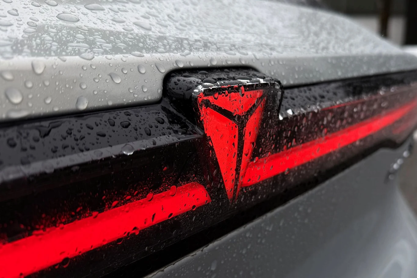 Changan Deepal S05 będzie jednym z dwóch SUV-ów, z którymi chiński producent zadebiutuje w Polsce. Logo samochodu w kształcie litery V podświetlone na czerwono, umieszczone na tylnej części srebrnego pojazdu pokrytego kroplami deszczu.