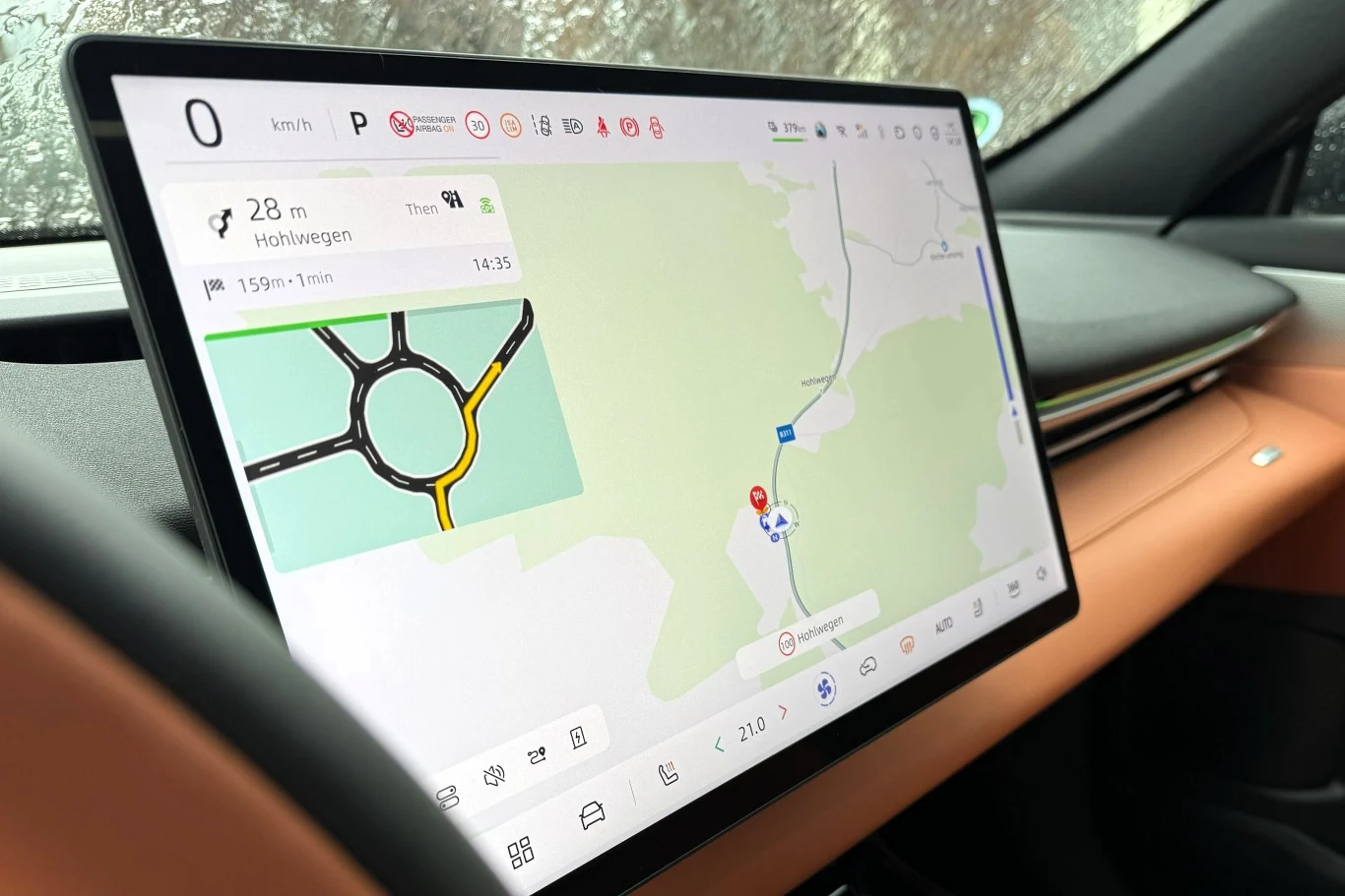 Jeśli nie chcemy korzystać z pokładowej nawigacji, możemy użyć naszej ulubionej aplikacji z mapami, łącząc nasz telefon za pośrednictwem Android Auto i Apple CarPlay. Duży ekran dotykowy w samochodzie pokazuje mapę nawigacji z trasą prowadzącą przez rondo, po prawej stronie widoczne są elementy wnętrza pojazdu w jasnobrązowym kolorze.
