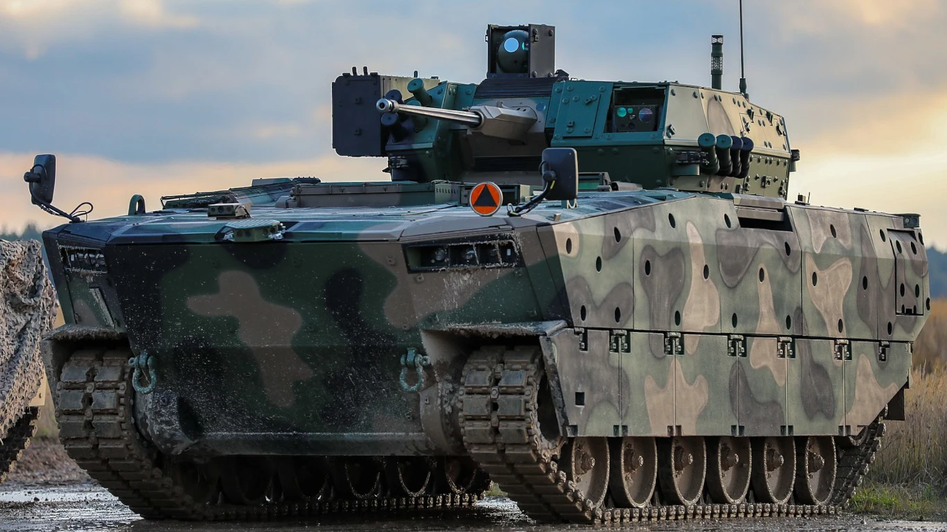 Nowoczesny bojowy wóz piechoty w kamuflażu, wyposażony w armatę automatyczną i sprzęt optoelektroniczny, stoi na utwardzonym terenie, gotowy do działania.