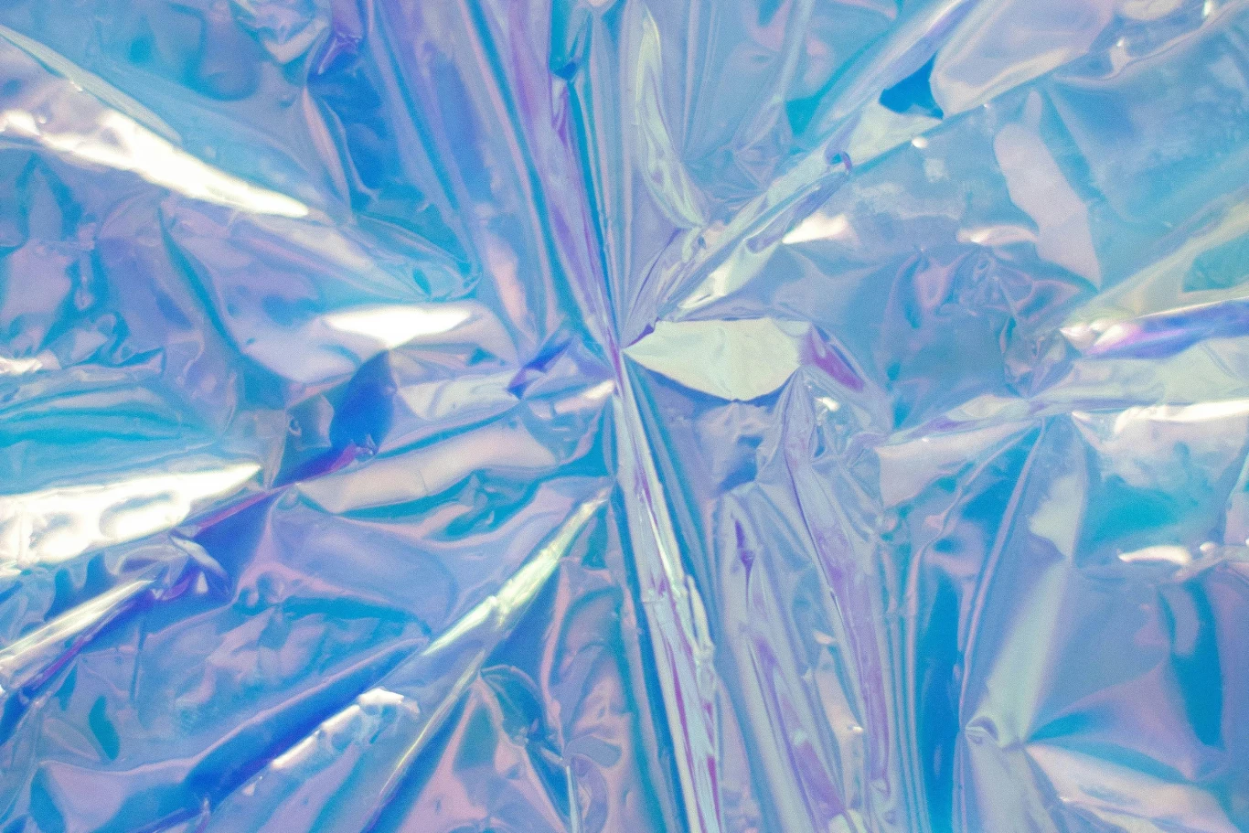 Biodegradowalna folia opakowaniowa zmniejsza zarówno przenikanie wilgoci, jak i tlenu. Lśniąca, kolorowa folia o perłowym połysku tworząca abstrakcyjny wzór z załamaniami i refleksami światła w odcieniach fioletu i błękitu.