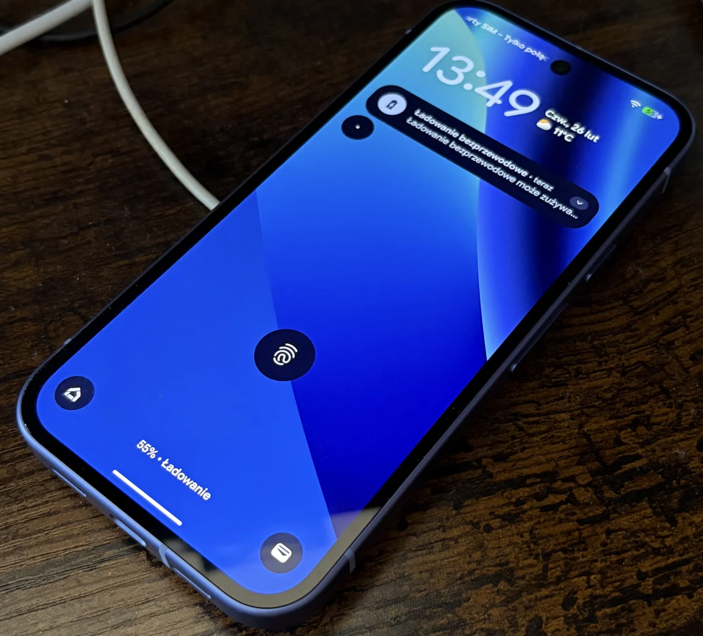 Smartfon z niebieskim ekranem blokady leżący na ciemnym drewnianym blacie, widoczny jest czas, powiadomienie oraz ikona odblokowania.