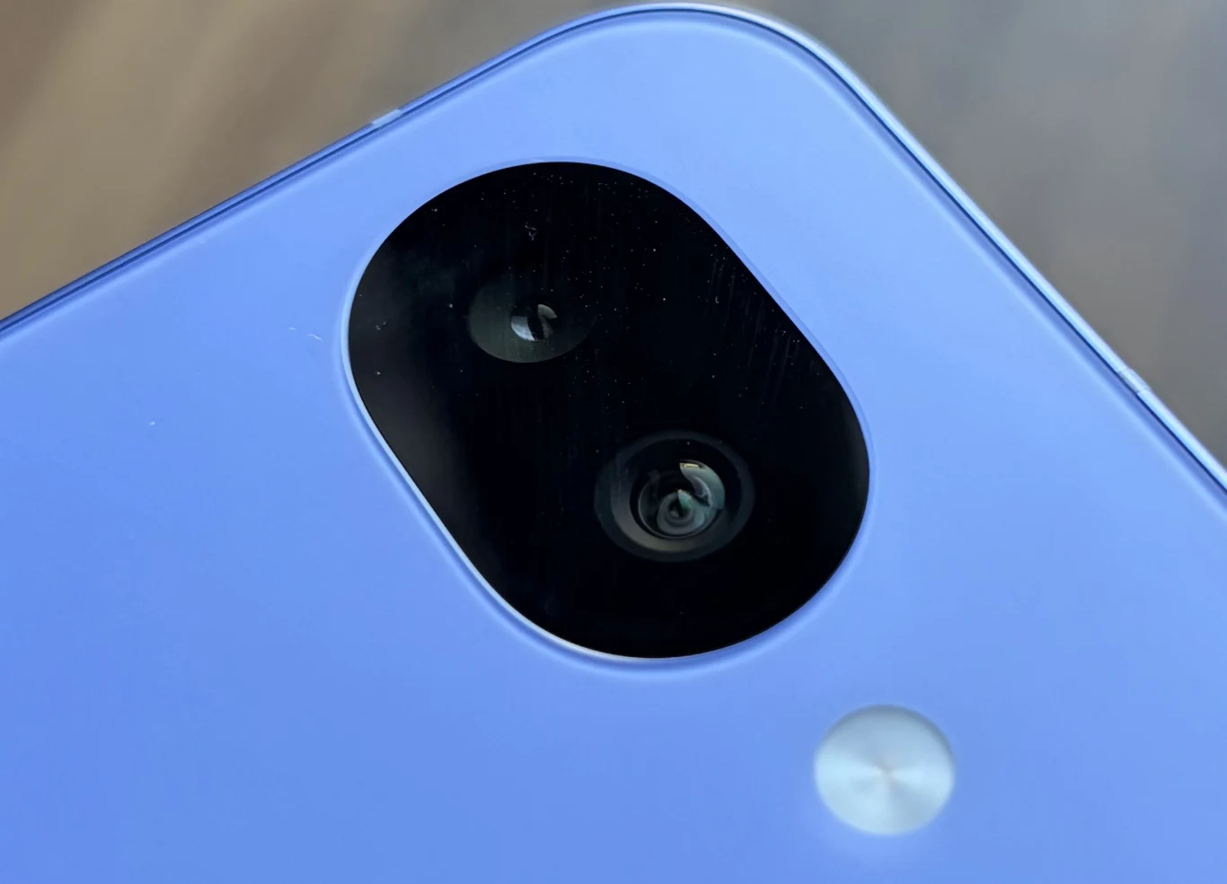 Zbliżenie na wyspę aparatów smartfona w niebieskiej obudowie, z dwoma obiektywami i lampą błyskową na tle rozmytego tła.