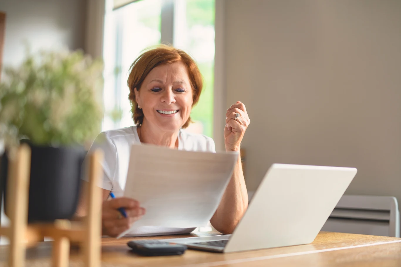 happy senior woman calculating family budget, sitting at kitchen counter with laptop, papers,