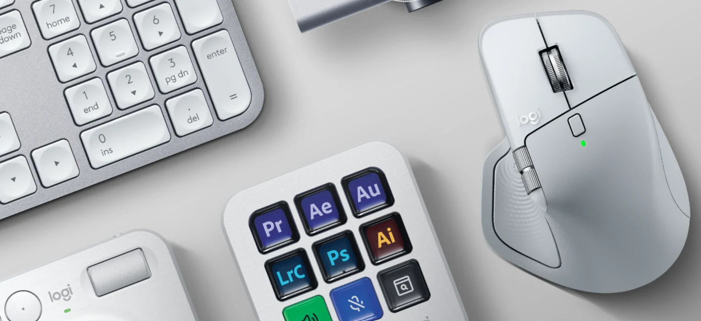 Biała mysz komputerowa z dodatkowym przyciskiem bocznym leży obok białej klawiatury oraz panelu z kolorowymi przyciskami z ikonami popularnych programów graficznych i montażowych.