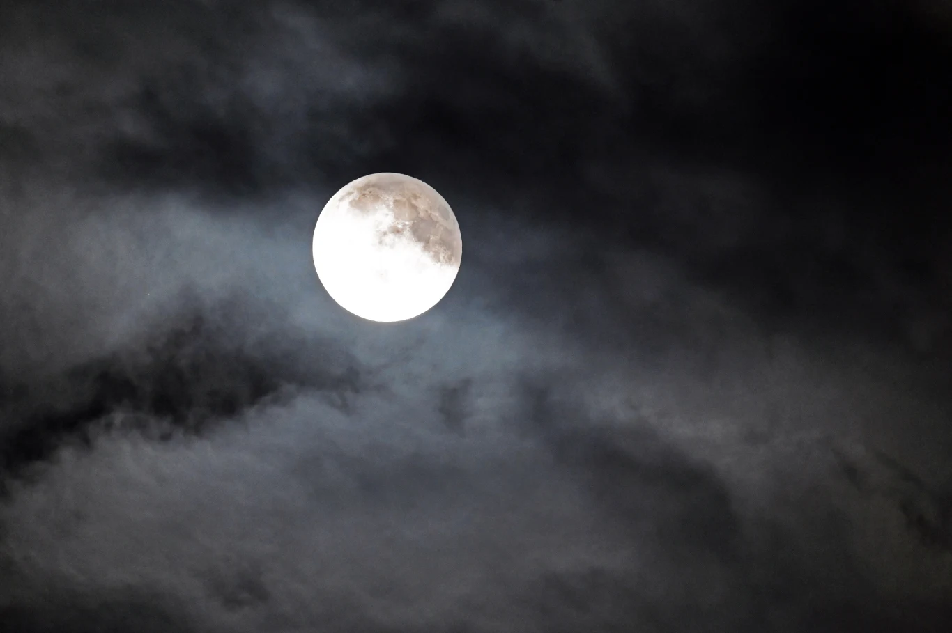 Jasny księżyc w pełni otoczony ciemnymi, przysłaniającymi go chmurami na nocnym niebie.