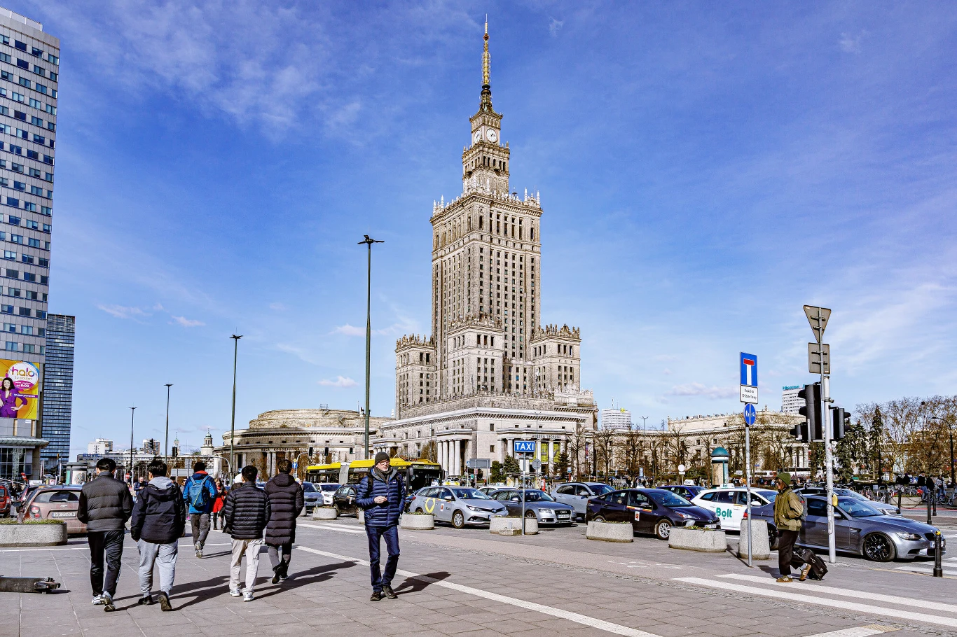 Polska znalazła się w gronie państw UE z najniższą luką płacową Pałac Kultury i Nauki dominuje nad centrum Warszawy, wokół którego poruszają się piesi i samochody w tętniącej życiem miejskiej scenerii. Po prawej stronie widoczny znak drogowy i liczba aut na jezdni, część budynków w tle oraz błękitne niebo z delikat...
