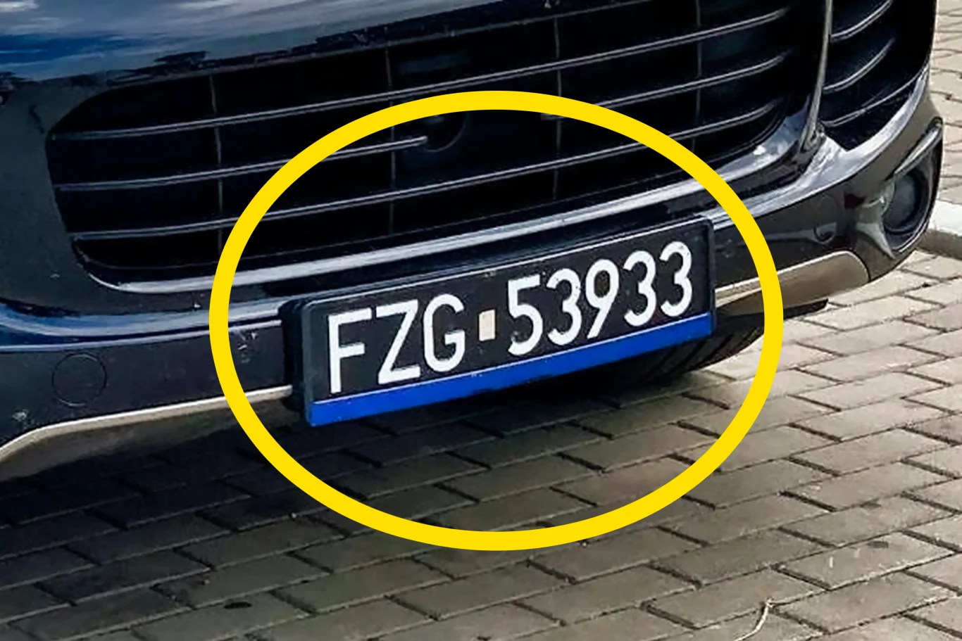 Czarne tablice rejestracyjne na współczesnym samochodzie. O co tu chodzi? Czarny samochód zbliżony od przodu, z wyeksponowaną tablicą rejestracyjną FZG 53933, tablica otoczona żółtym okręgiem, samochód stoi na kostce brukowej.