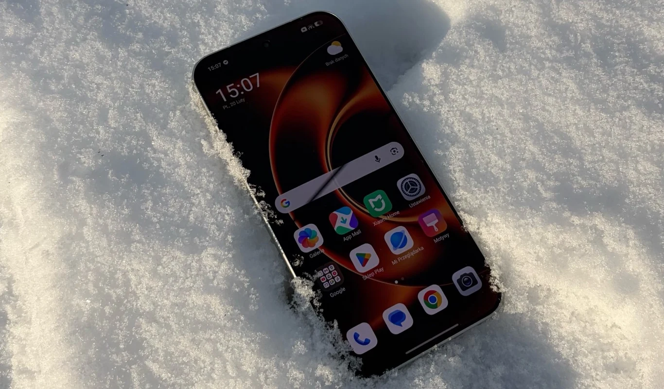Nowoczesny smartfon z wyświetlaczem dotykowym leżący w śniegu, na ekranie widoczne są ikony popularnych aplikacji.