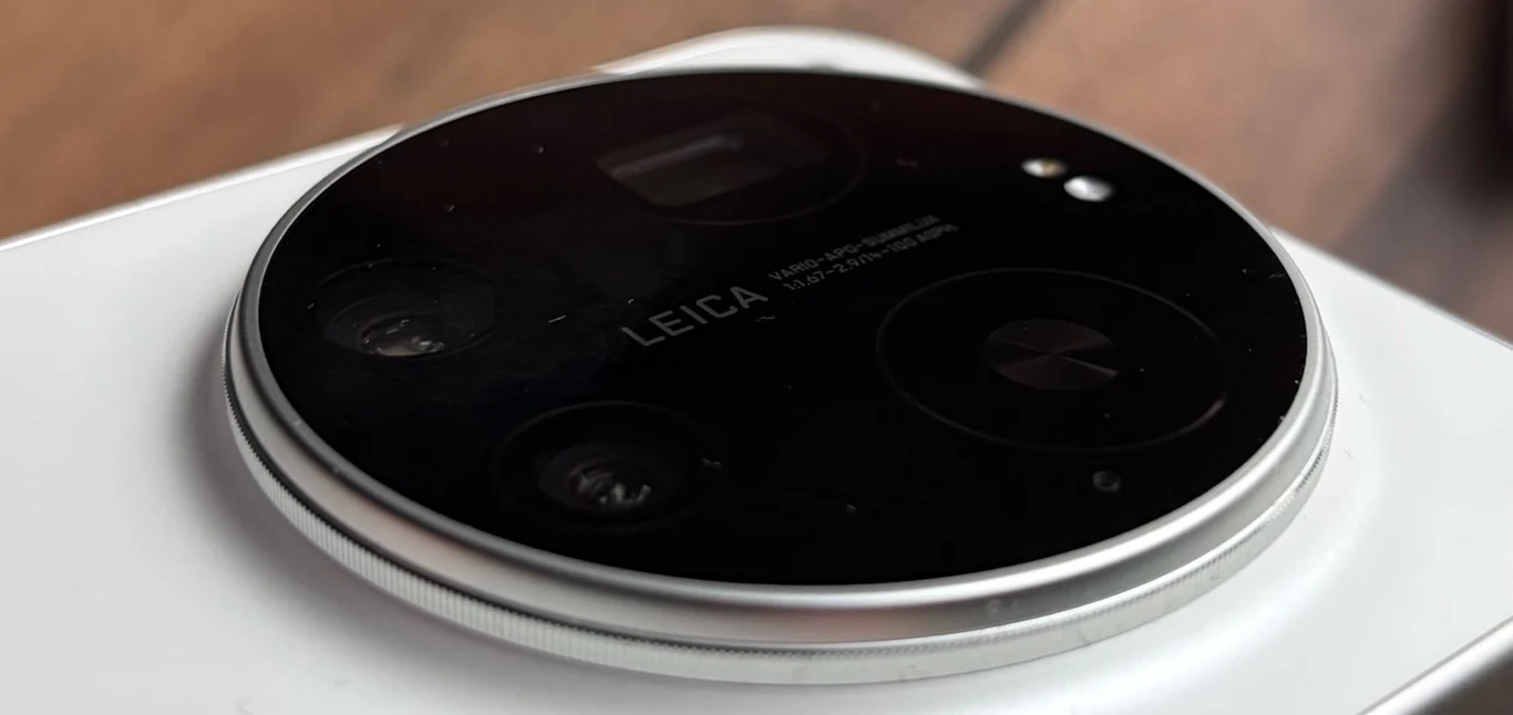 Moduł aparatu fotograficznego z trzema obiektywami i logo Leica na obudowie smartfona, wykończony metalową ramką. Tło jest rozmyte.