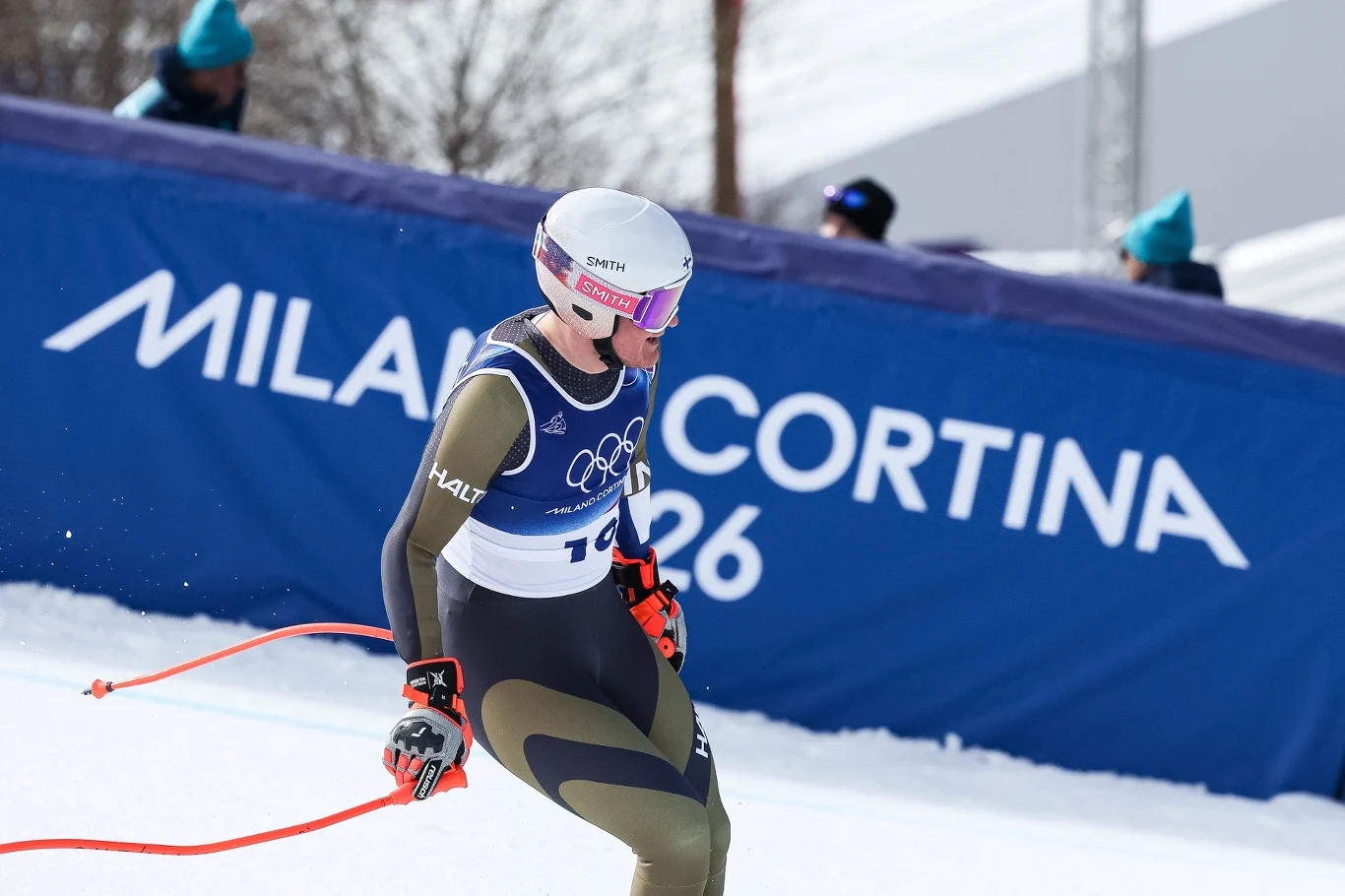 Elian Lehto Narciarz alpejski ubrany w kombinezon startowy oraz kask z goglami w trakcie zawodów olimpijskich na trasie zjazdowej, w tle baner z napisem Milano Cortina 2026.