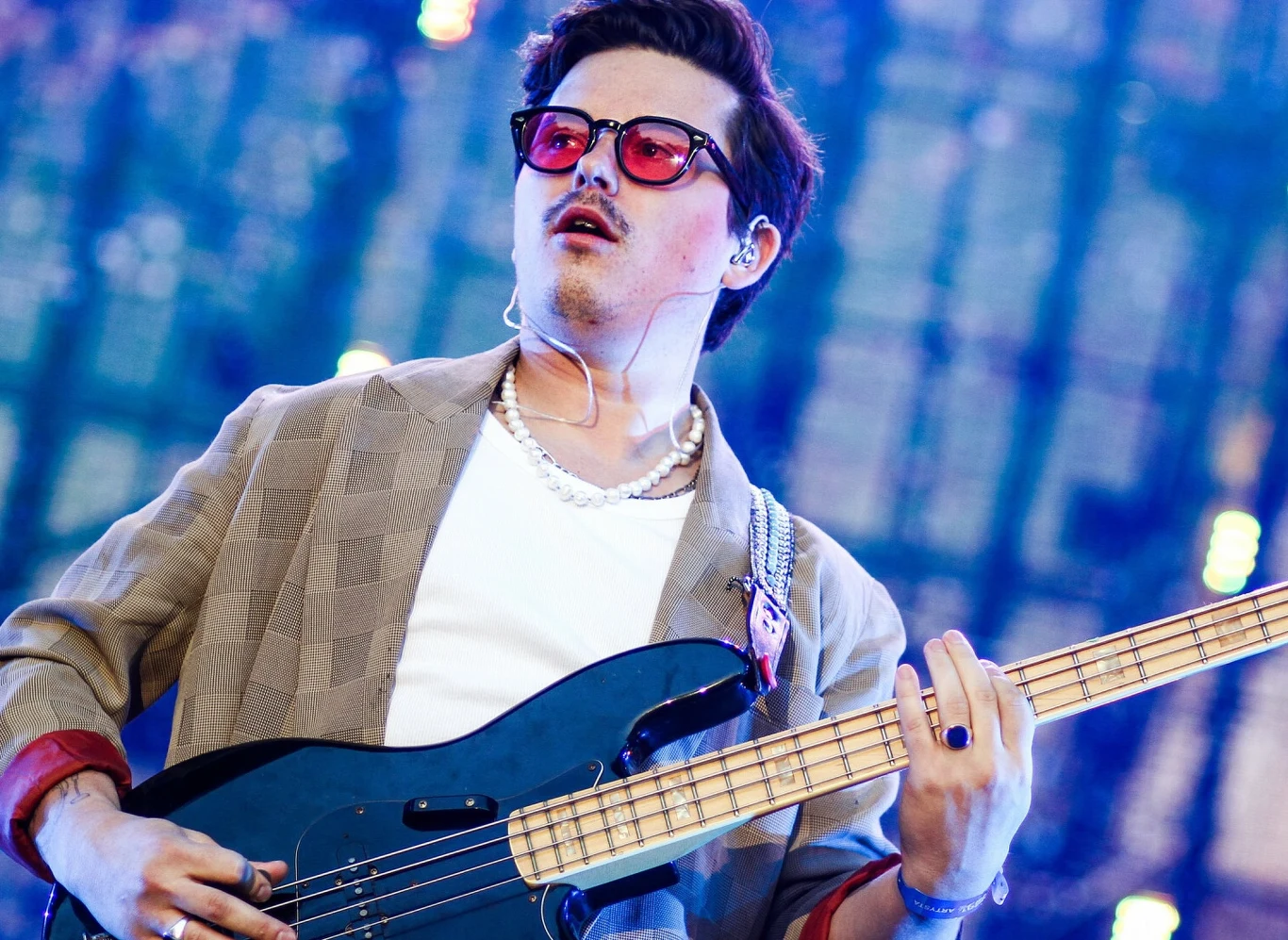 Kuba Karaś zdementował plotki o związku z Julią Wieniawą Mężczyzna w okularach i perłowym naszyjniku grający na gitarze basowej podczas koncertu, kolorowe rozmyte światła w tle podkreślają atmosferę wydarzenia muzycznego.