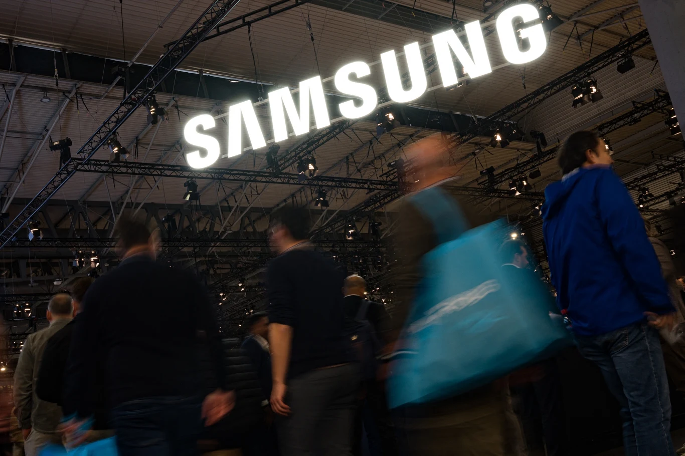 Samsung zamyka ostatnią fabrykę telewizorów na Słowacji. Zdj. ilustracyjne Tłum ludzi w hali wystawowej z widocznym dużym, podświetlonym logo firmy Samsung nad głowami uczestników.