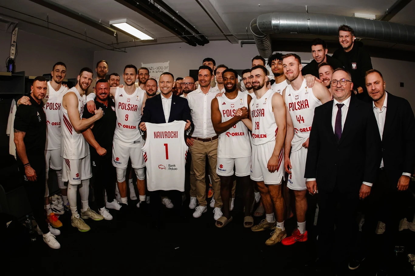 Karol Nawrocki otrzymał od "KoszKadry" specjalną koszulkę ze swoim nazwiskiem Grupa uśmiechniętych zawodników polskiej drużyny koszykarskiej pozuje w szatni wraz ze sztabem trenerskim i oficjelami, na środku widoczna koszulka z nazwiskiem Wójcik.