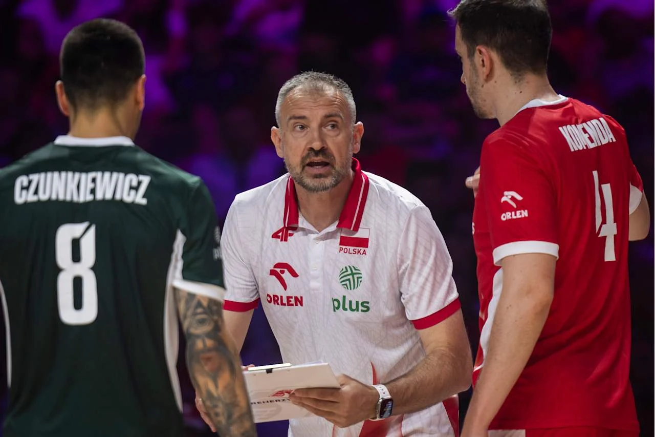 Trener reprezentacji Polski podczas omawiania strategii z dwoma siatkarzami ubranymi w stroje meczowe, jeden w zielonej koszulce z numerem 8 i nazwiskiem Czunkiewicz, drugi w czerwonej z numerem 4 i nazwiskiem Kochanowski, wyraźne skupienie na twarzach...