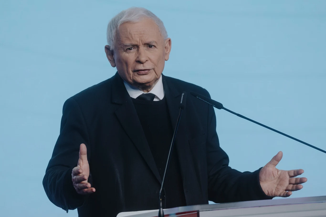 Czy Jarosław Kaczyński rzeczywiście znalazł już pewnego kandydata na premiera? Starszy mężczyzna w ciemnym garniturze, białej koszuli i swetrze stoi za mównicą, gestykuluje obiema rękoma, patrzy przed siebie. W tle jasne, jednolite tło, przy mównicy mikrofon.