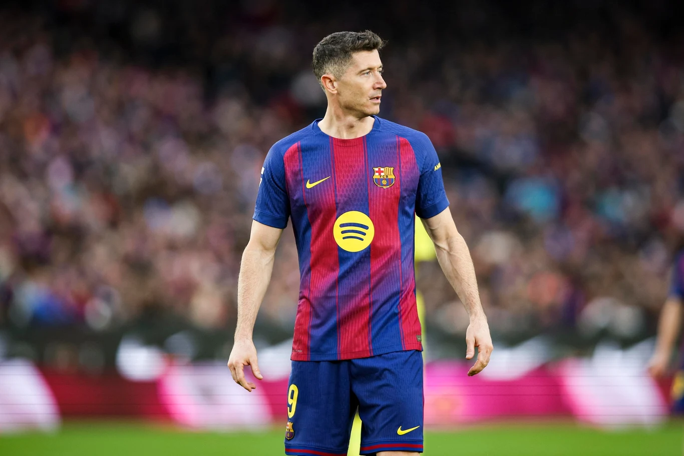 Piłkarz w koszulce FC Barcelony na tle stadionu podczas meczu, widoczny numer 9 oraz logo sponsora na koszulce, w tle rozmyta publiczność.