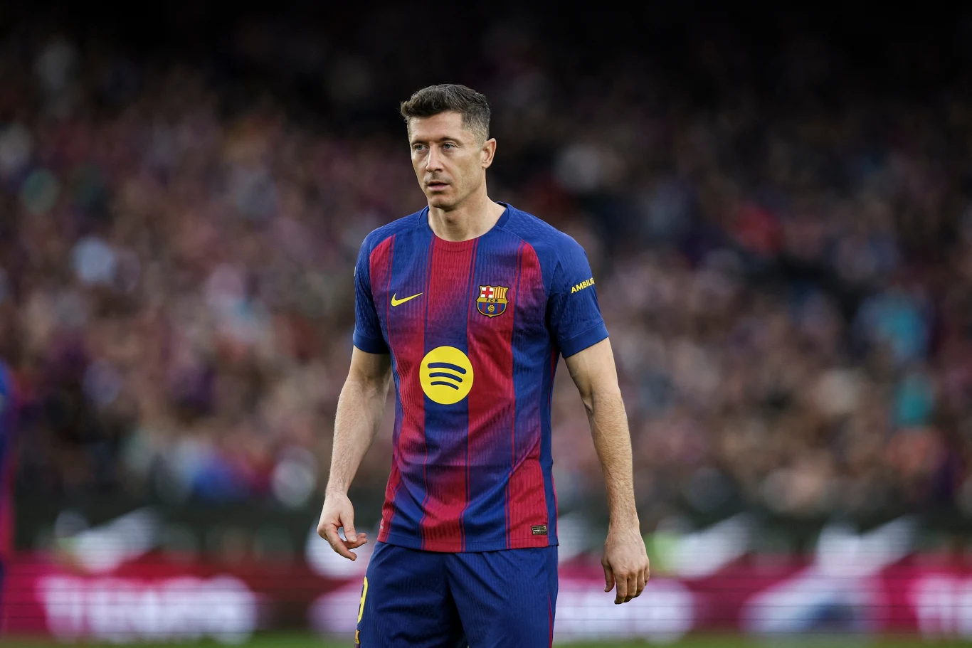 Robert Lewandowski Piłkarz w stroju FC Barcelony stoi na boisku w czasie meczu, na tle rozmytej publiczności.