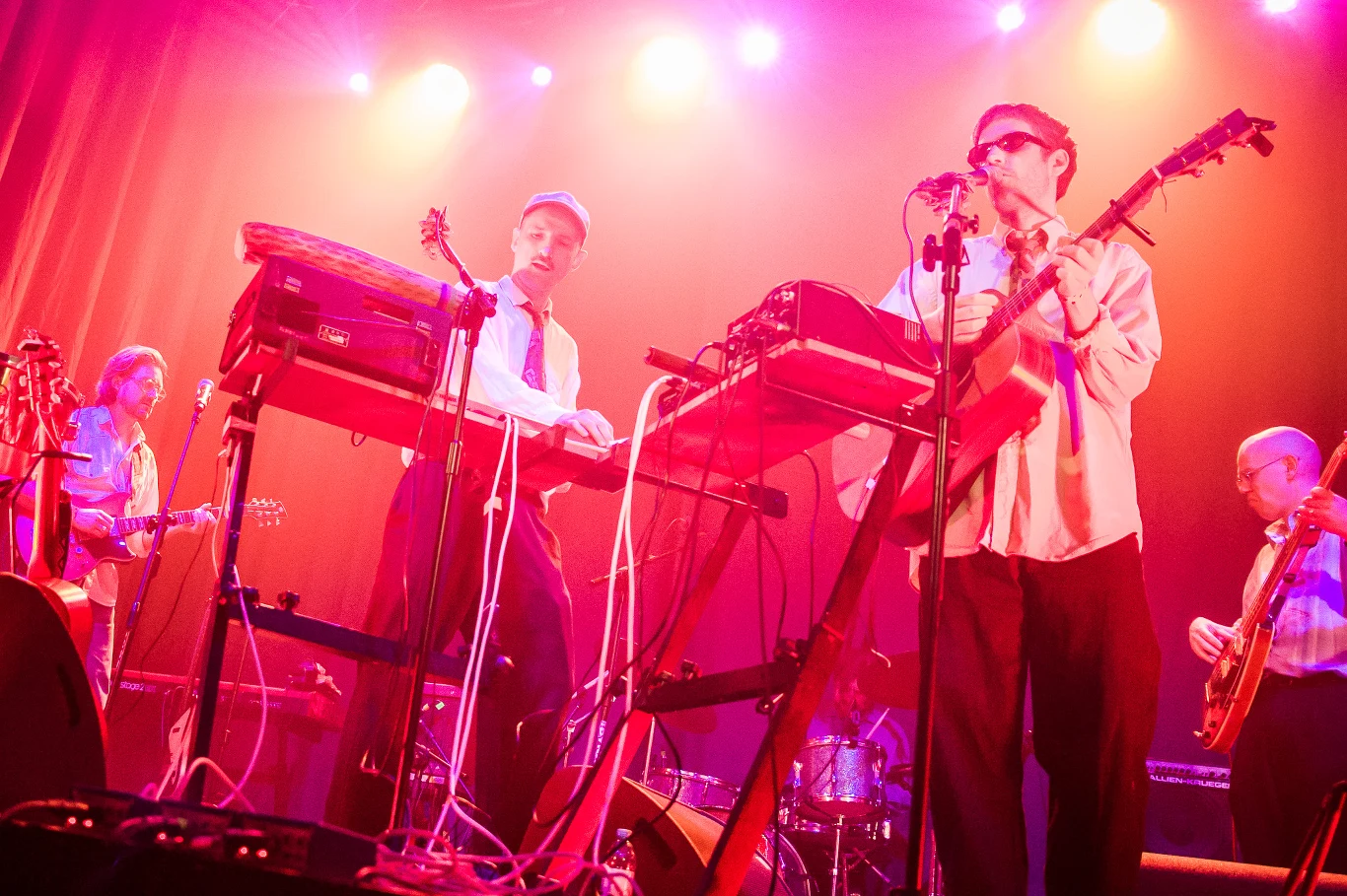 Bigga Fest: Grupa Torpedo Zespół muzyczny wykonujący utwory na scenie, otoczony intensywnym różowym oświetleniem, z widocznymi instrumentami klawiszowymi, gitarami i mikrofonami, muzycy w eleganckich strojach grają i śpiewają.