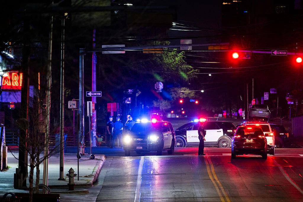 USA. Atak w Austin w Teksasie, są zabici i ranni. "Akt terroryzmu" Radiowozy policyjne z włączonymi światłami stoją na zamkniętej ulicy nocą, kilku funkcjonariuszy policji kontroluje sytuację na środku skrzyżowania.