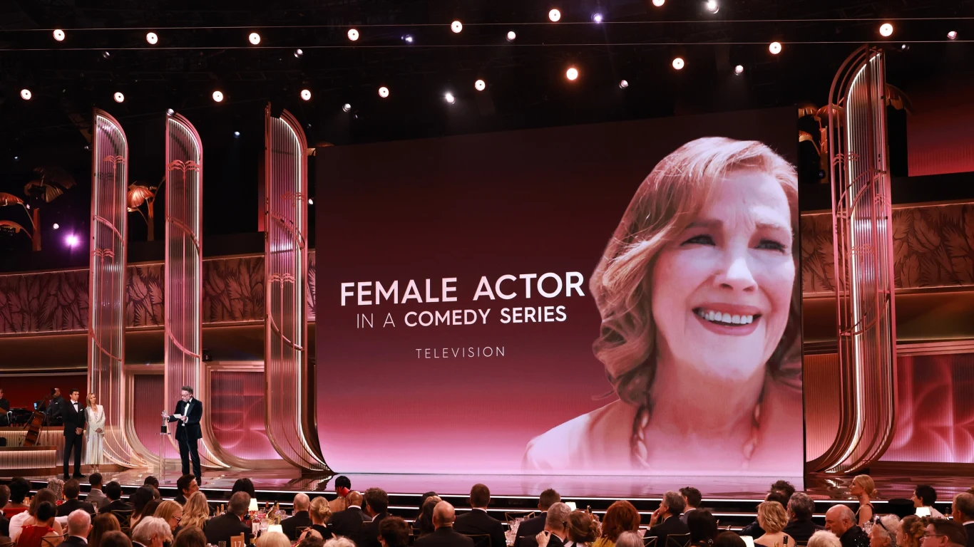 Uroczysta gala wręczenia nagród, publiczność siedzi przed dużym ekranem z napisem informującym o kategorii nagrody aktorskiej w serialu komediowym, na ekranie widoczny portret uśmiechniętej kobiety.