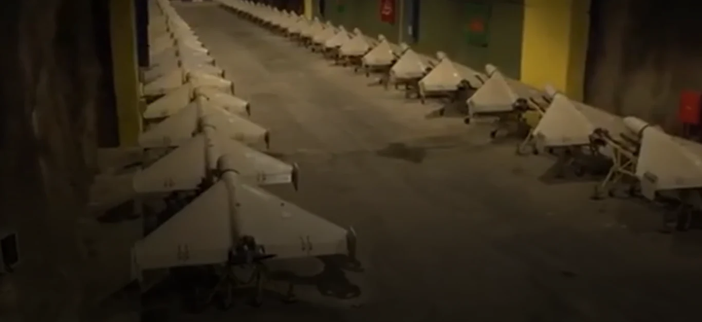 Shahed-136 w roli głównej. Iran pokazał podziemne tunele pełne dronów Rząd wojskowych dronów ustawionych w szeregu wewnątrz oświetlonego pomieszczenia, surowe betonowe ściany i podłoga tworzą klimat podziemnego bunkra.