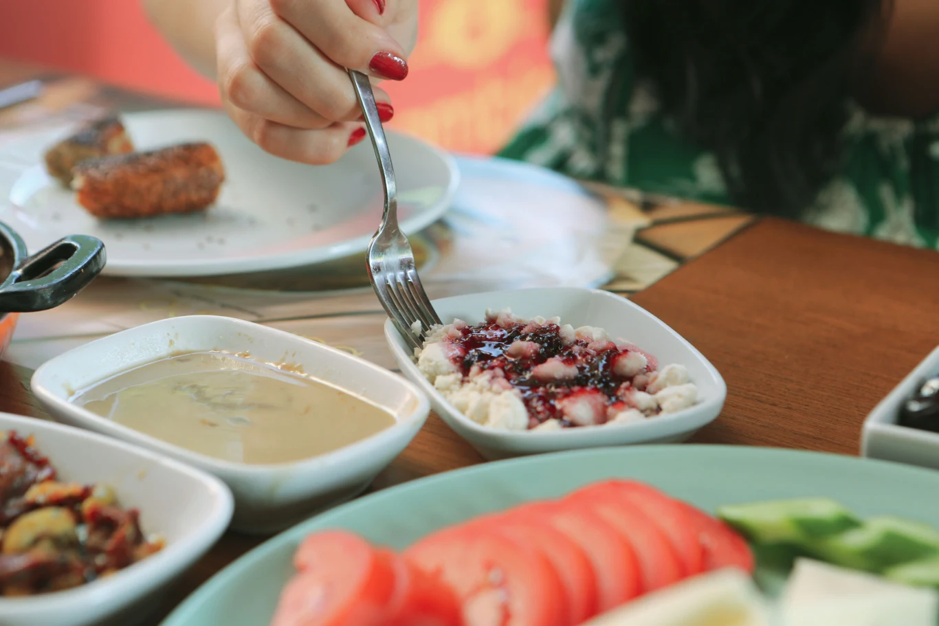 Kolacja powinna być lekka i umiarkowana objętościowo Ręka z widelcem sięga po twaróg z konfiturą, obok miseczka z sosem, na pierwszym planie pokrojone pomidory i ogórki, w tle panierowany kotlet na białym talerzu.