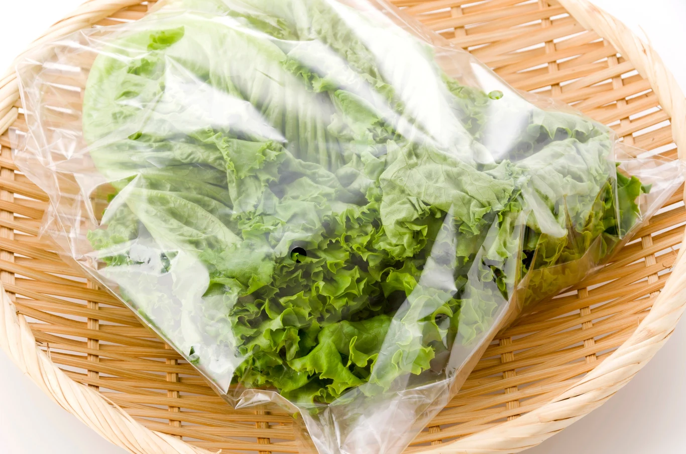 Sałata zapakowana w przezroczystą folię na okrągłym wiklinowym talerzu.