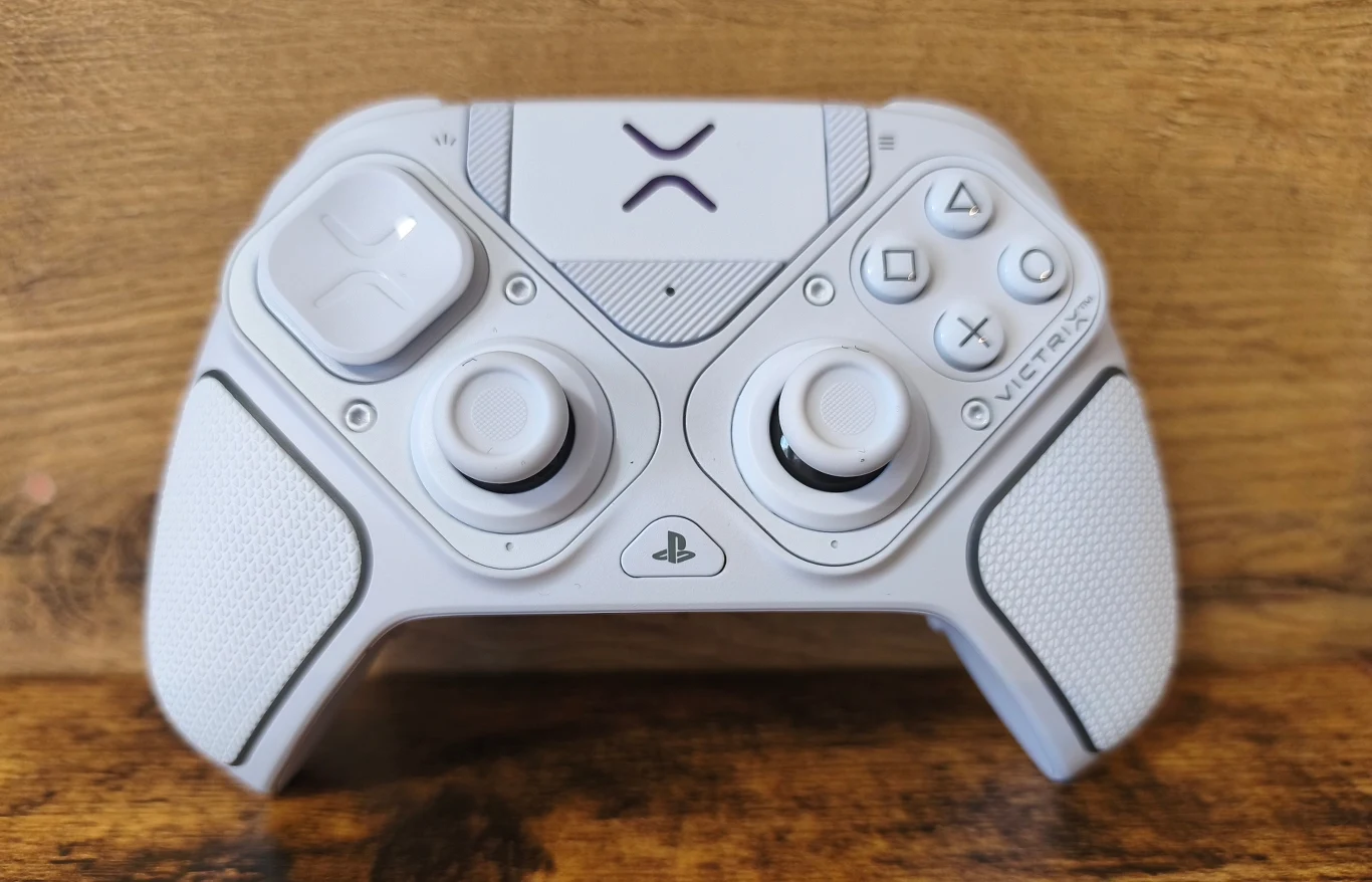 Biały kontroler do konsoli PlayStation z dwoma gałkami analogowymi, czterema przyciskami akcji po prawej stronie, krzyżakiem po lewej i widocznym logo PlayStation na środku, umieszczony na drewnianej powierzchni.