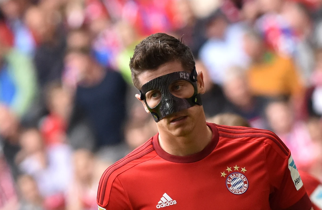 Robert Lewandowski, 09.05.2015 r. Piłkarz w czerwonym stroju Bayernu Monachium, z czarną ochronną maską na twarzy, stoi na boisku podczas meczu, otoczony rozmytym tłumem kibiców w tle.
