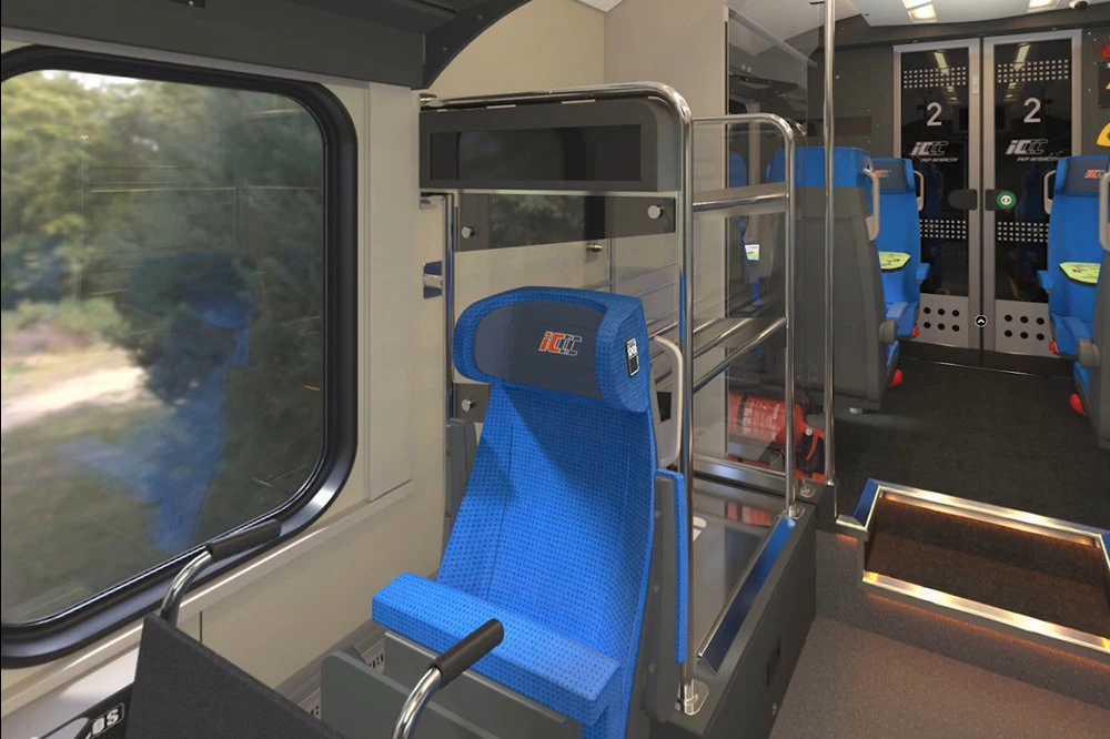 Przestrzeń wewnątrz nowoczesnego wagonu kolejowego z wyznaczonym miejscem dla osób niepełnosprawnych oraz widocznym miejscem na wózek inwalidzki, obok szerokiego okna i jasno-niebieskich foteli pasażerskich w dalszej części wagonu.