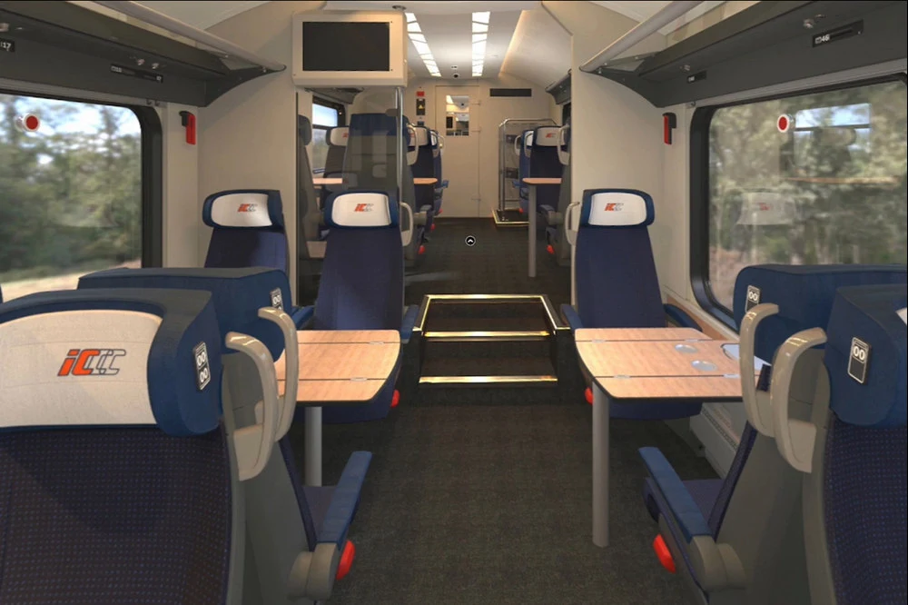 Wnętrze nowoczesnego wagonu kolejowego z wygodnymi, granatowymi fotelami ustawionymi po obu stronach przejścia, stolikami przy siedzeniach oraz dużymi oknami po bokach.