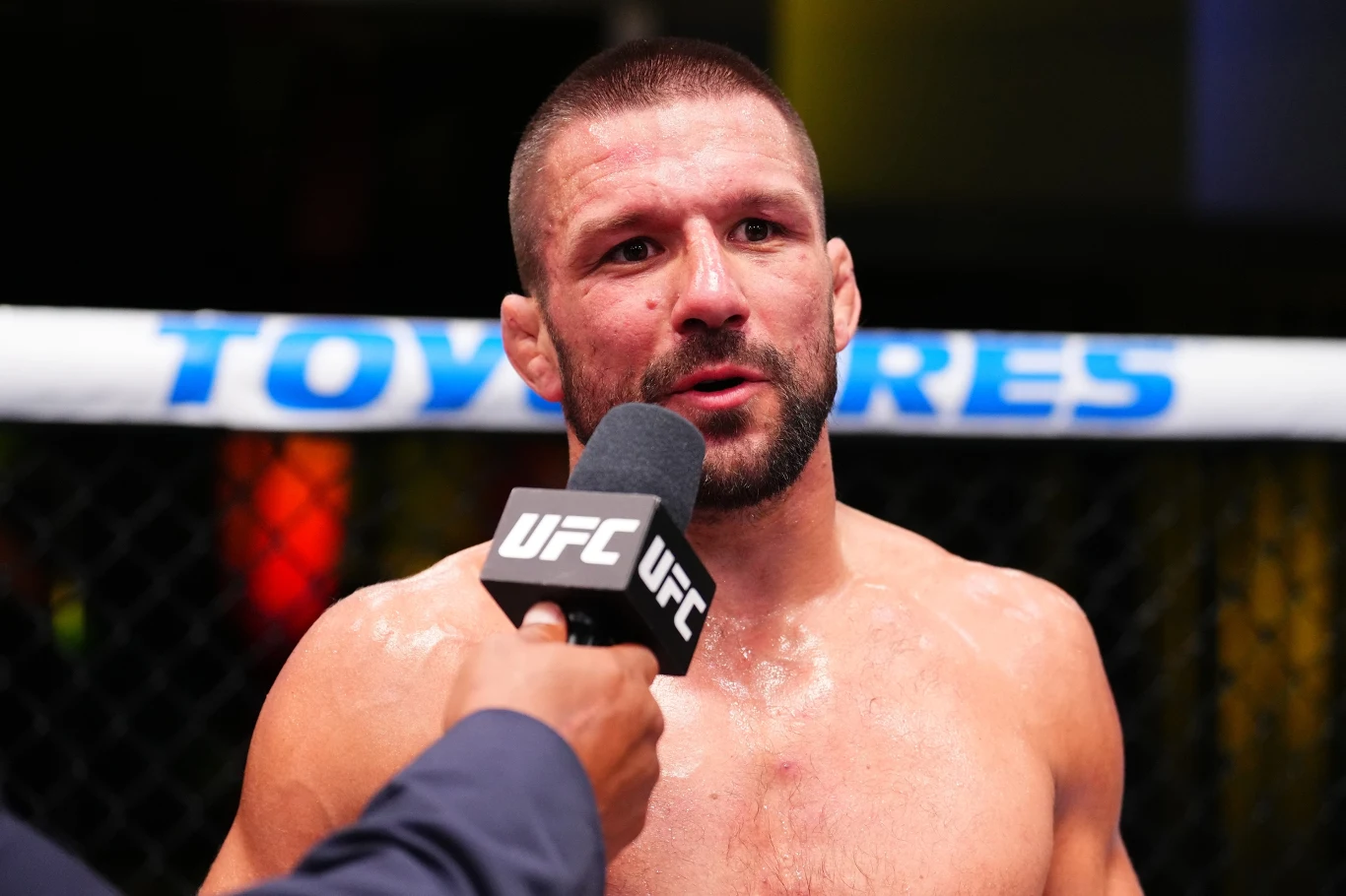 Mateusz Gamrot Mateusz Gamrot podczas wywiadu po walce w oktagonie UFC, trzyma mikrofon, widoczne ślady potu i wysiłku.