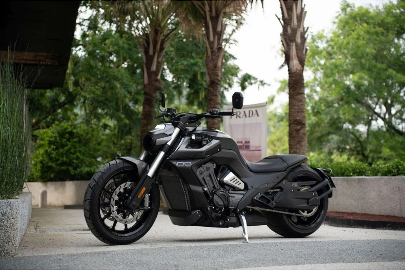 Czarny motocykl sportowy o nowoczesnym designie stoi zaparkowany na tle palm i zieleni, wyróżniając się solidną sylwetką oraz dużymi kołami.