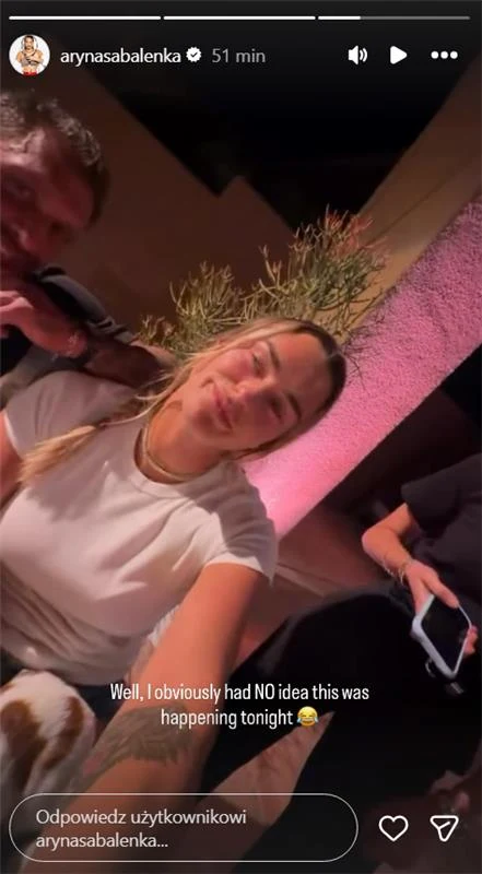 Aryna Sabalenka się zaręczyła, ale nie była do końca zadowolona Młoda kobieta uśmiecha się, siedząc w towarzystwie innych osób przy stole w ciepłym, przytulnym otoczeniu z rośliną ozdobną i różowo oświetloną ścianą w tle.