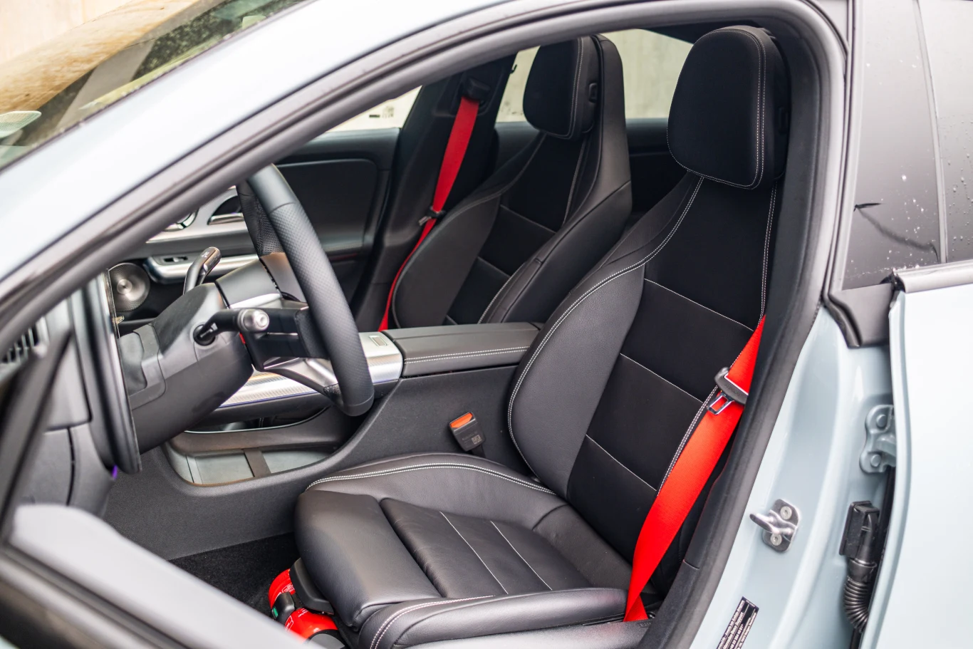 Fotele są wygodne, choć sama ich pozycja nie jest tak niska, jak niektórzy by oczekiwali. Wnętrze nowoczesnego samochodu z czarnymi skórzanymi fotelami i czerwonymi pasami bezpieczeństwa, elegancka deska rozdzielcza oraz sportowe wykończenia detali.