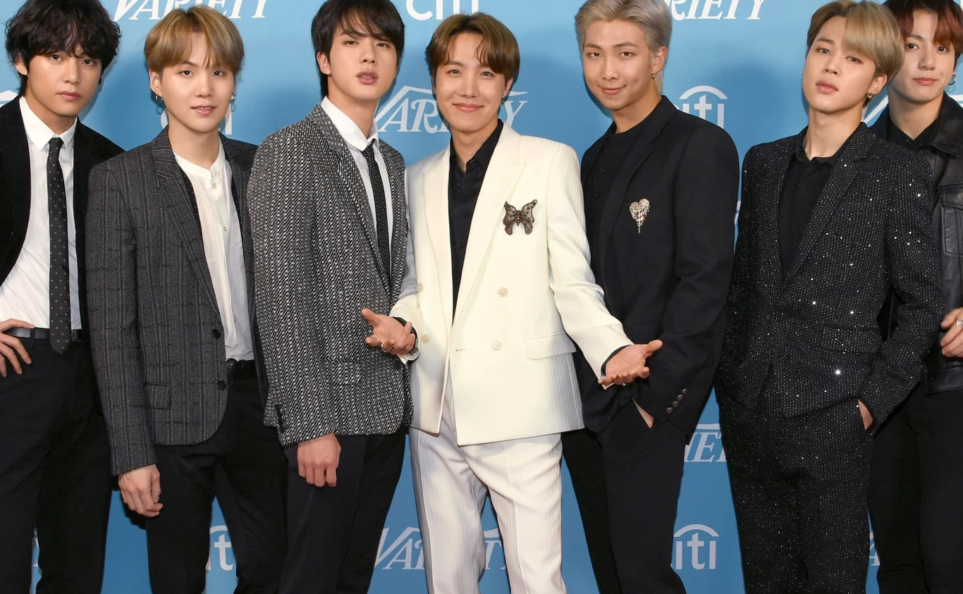 BTS (od lewej): V, Suga, Jin, J-Hope, RM, Jimin i Jungkook Zespół BTS pozuje na niebieskiej ściance. od lewej: V, Suga, Jin, J-Hope, RM, Jimin i Jungkook