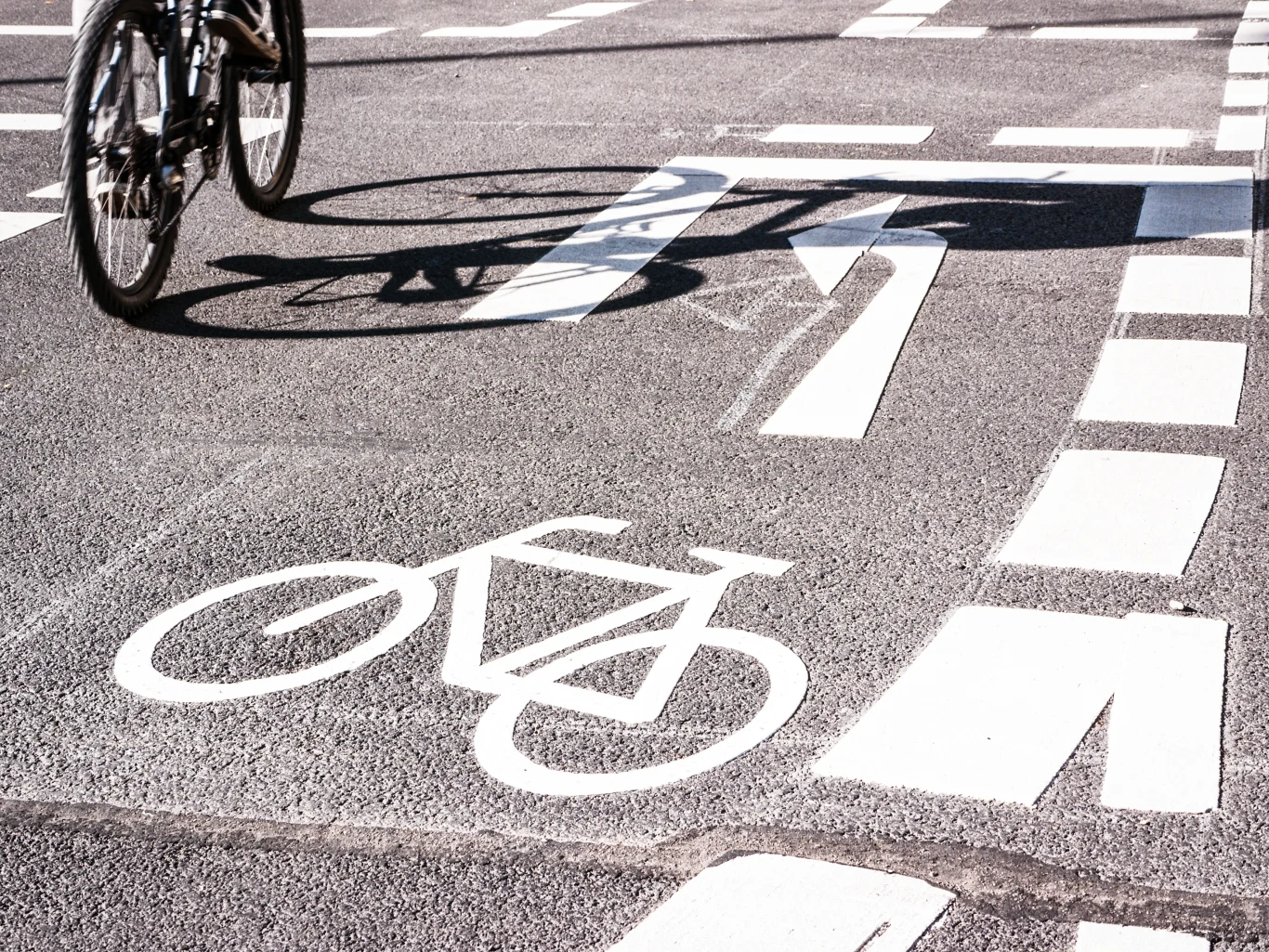Fragment jezdni z wyznaczoną drogą rowerową, oznaczoną białym piktogramem roweru i wyraźnymi liniami, po której jedzie rowerzysta.