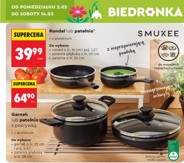 Patelnie i rondle SMUKEE z powłoką nieprzywierającą oraz garnek z pokrywką w promocji od 39,99 zł, źródło: gazetka Biedronka, str. 12 Oferta promocyjna naczyń kuchennych z serii Smukee obejmująca rondle, patelnie i garnki aluminiowe z nieprzywierającą powłoką oraz pokrywką, prezentowane na drewnianej powierzchni z widocznymi cenami i hasłami reklamowymi, w tle grafika pomidorów oraz ...